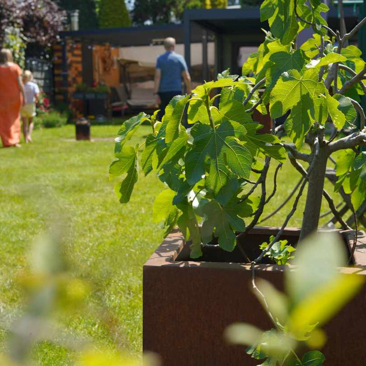Pflanzkübel aus Cortenstahl in einem Garten mit einer Familie dahinter