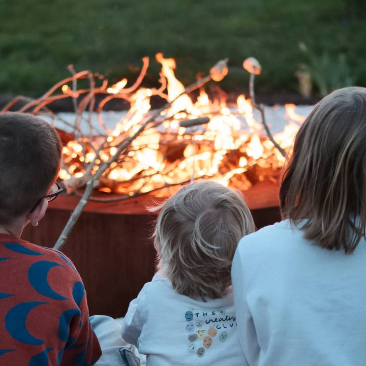 Kinder setzen am Feuer um eine Cortenstahl Schale