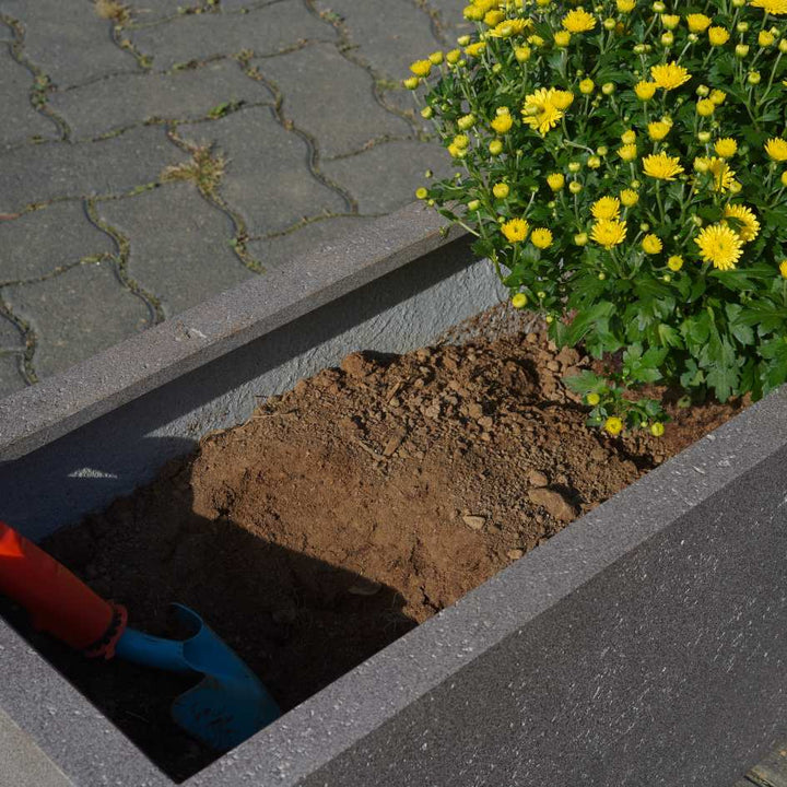 Eine Gartenschaufel liegt in einem halbbepflanzten Pflanzkübel aus Fiberglas