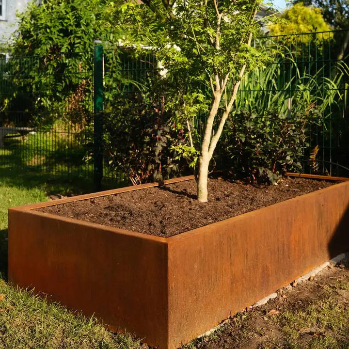Rechteckiges Hochbeet aus Cortenstahl in einem Garten mit einem Baum darin