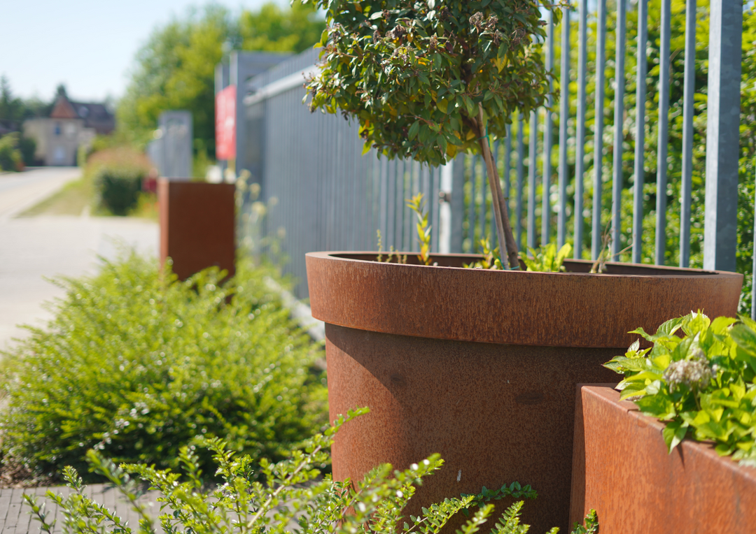 große, weiße Pflanzbehälter aus Metall in einem Innenhof