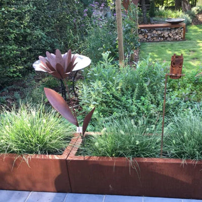 Rechteckiges Hochbeet aus Cortenstahl in einem grünen Garten mit vielen Dekoelementen